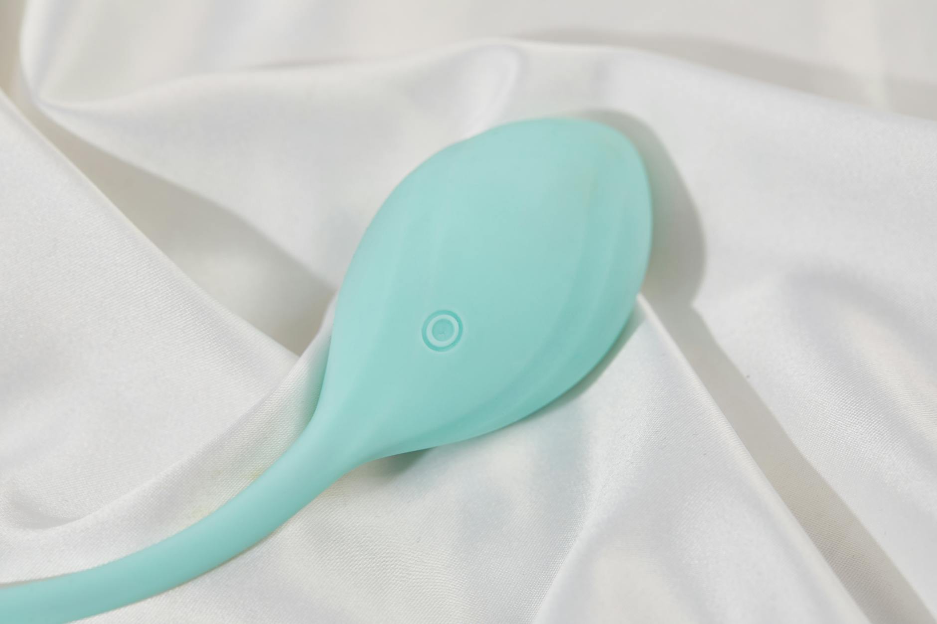 A teal vibrator on smooth white silk fabric, symbolizing sensuality and self-care during stressful times.