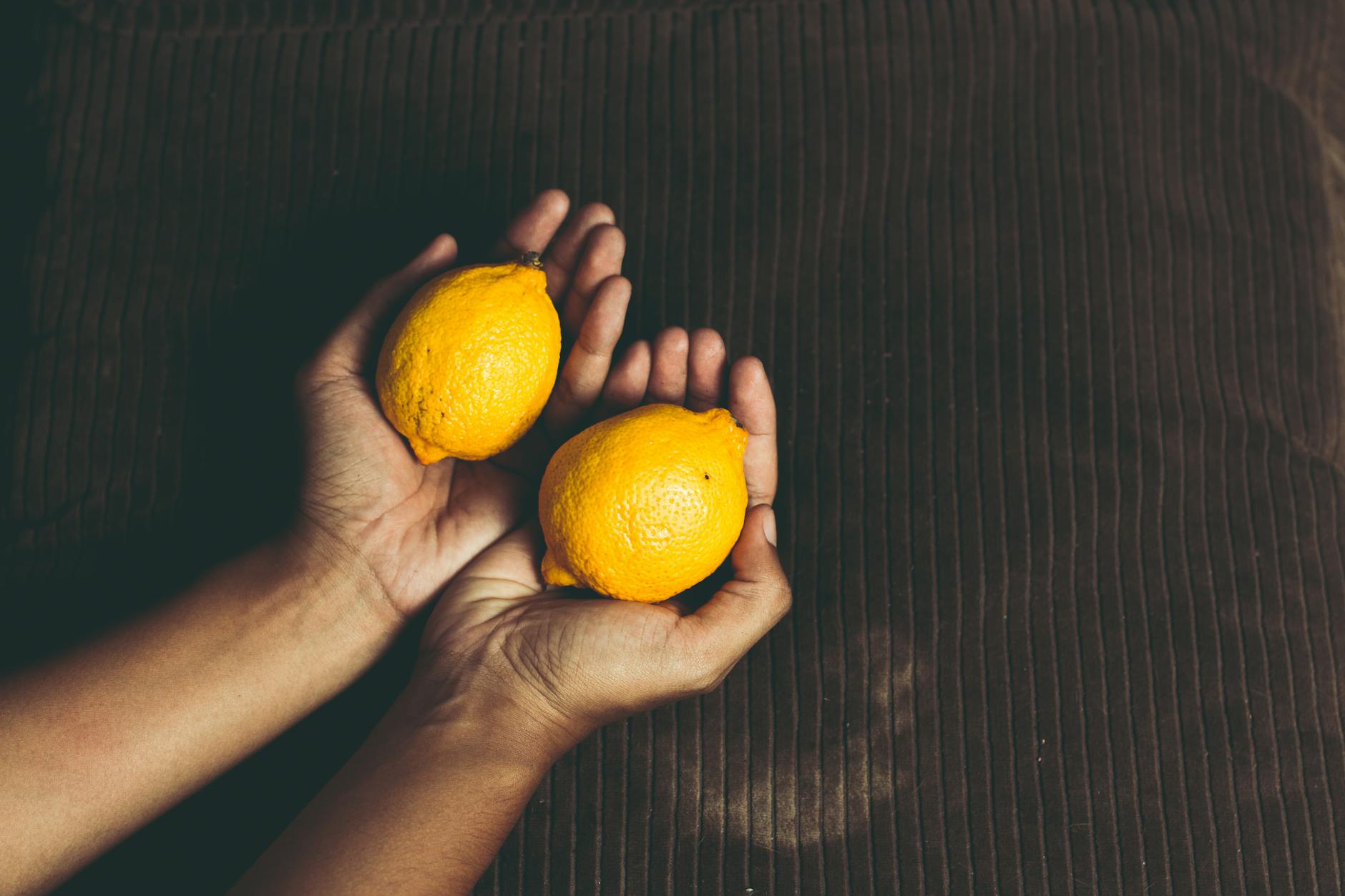A hand holding an orange vibrator against a minimalistic purple backdrop