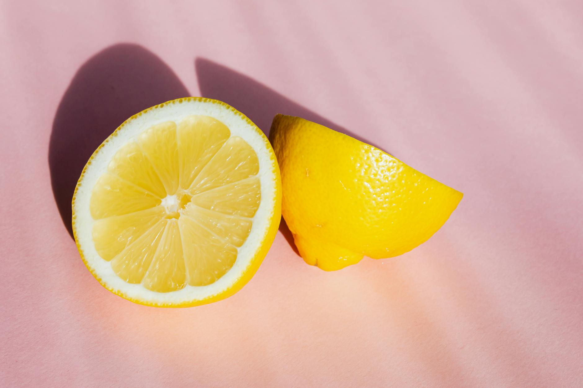 Fresh lemon halves on a pink background in sunlight, symbolizing natural stress relief