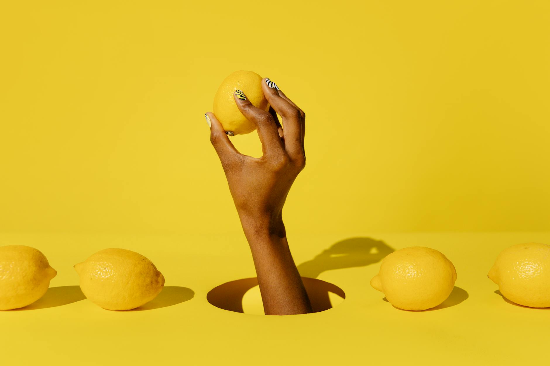 A close-up of a hand holding a fresh lemon against a vivid yellow background, conveying freshness and citrusy energy.