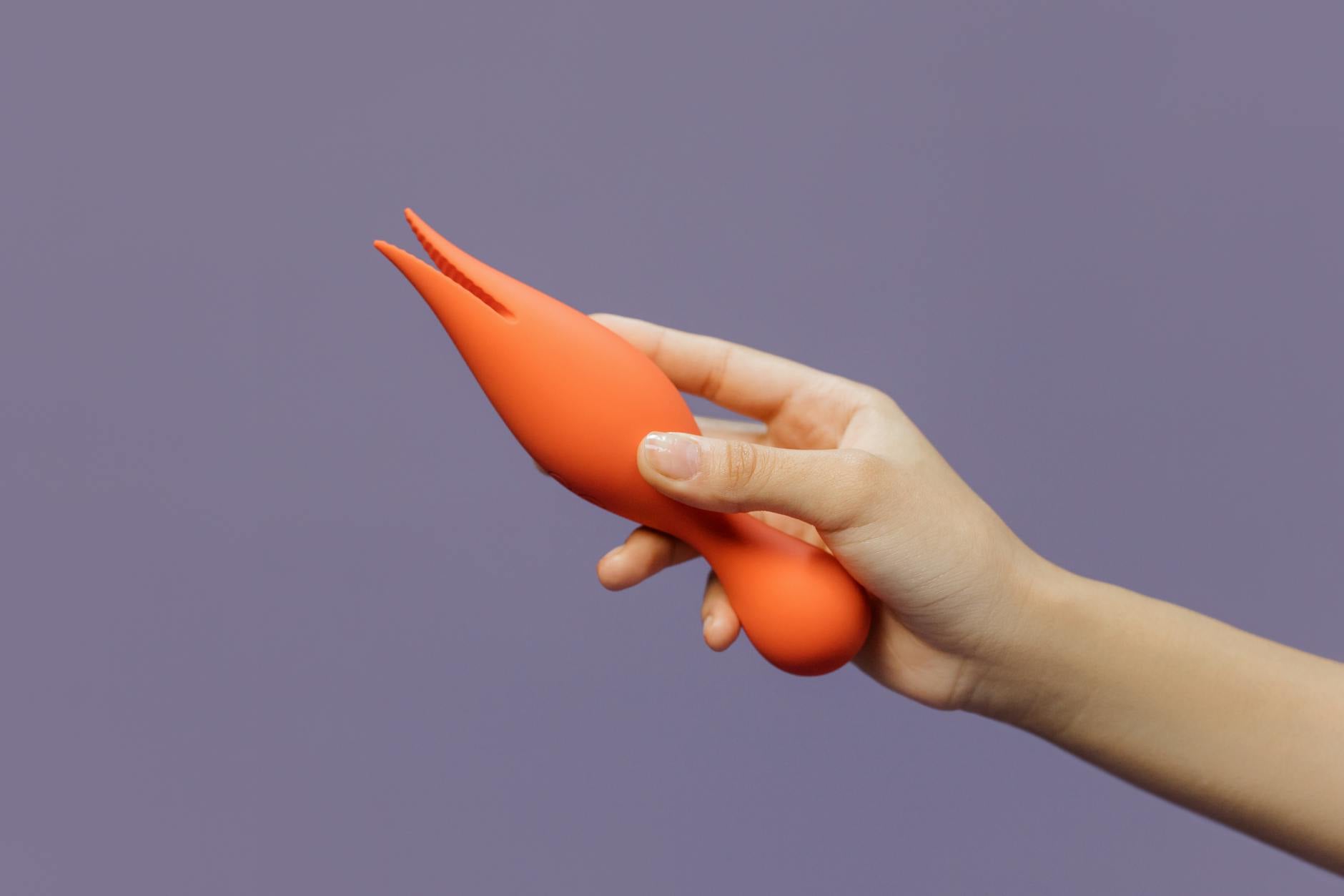 Close-up of a hand holding a lemon vibrator against a minimalistic purple backdrop, showcasing gentle sensuality