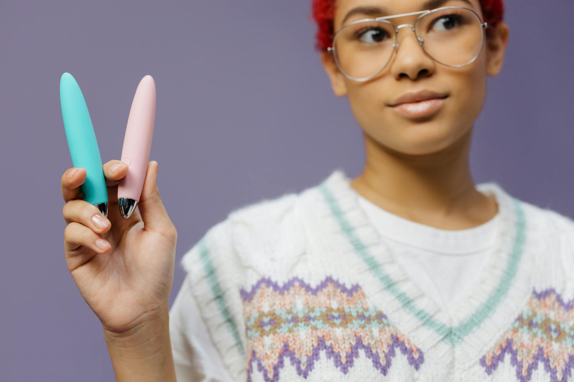 A woman holds a vibrant clitoral vibrator against a purple background, representing self-advocacy and pleasure in partnership.