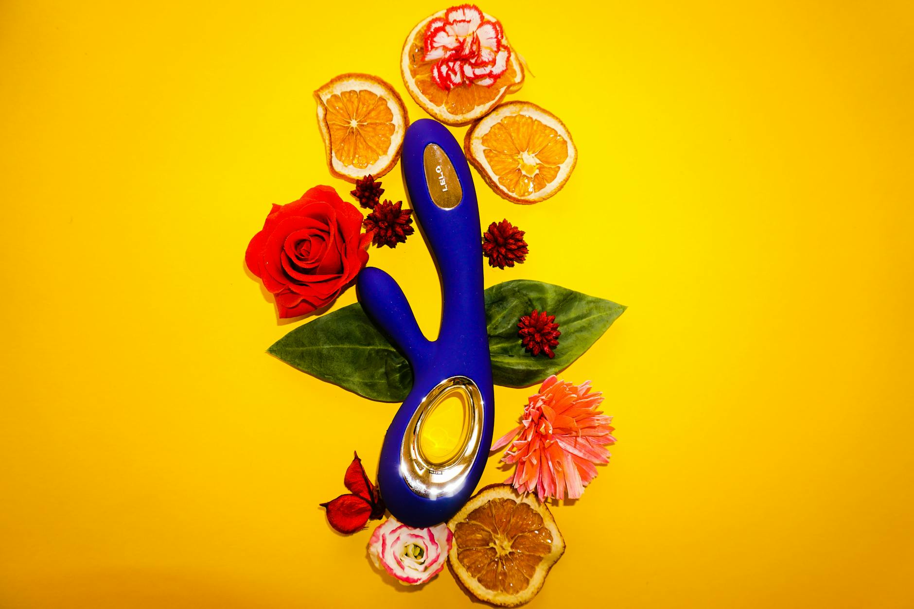 A blue clitoral vibrator surrounded by fresh lemons and citrus elements on a bright yellow background.