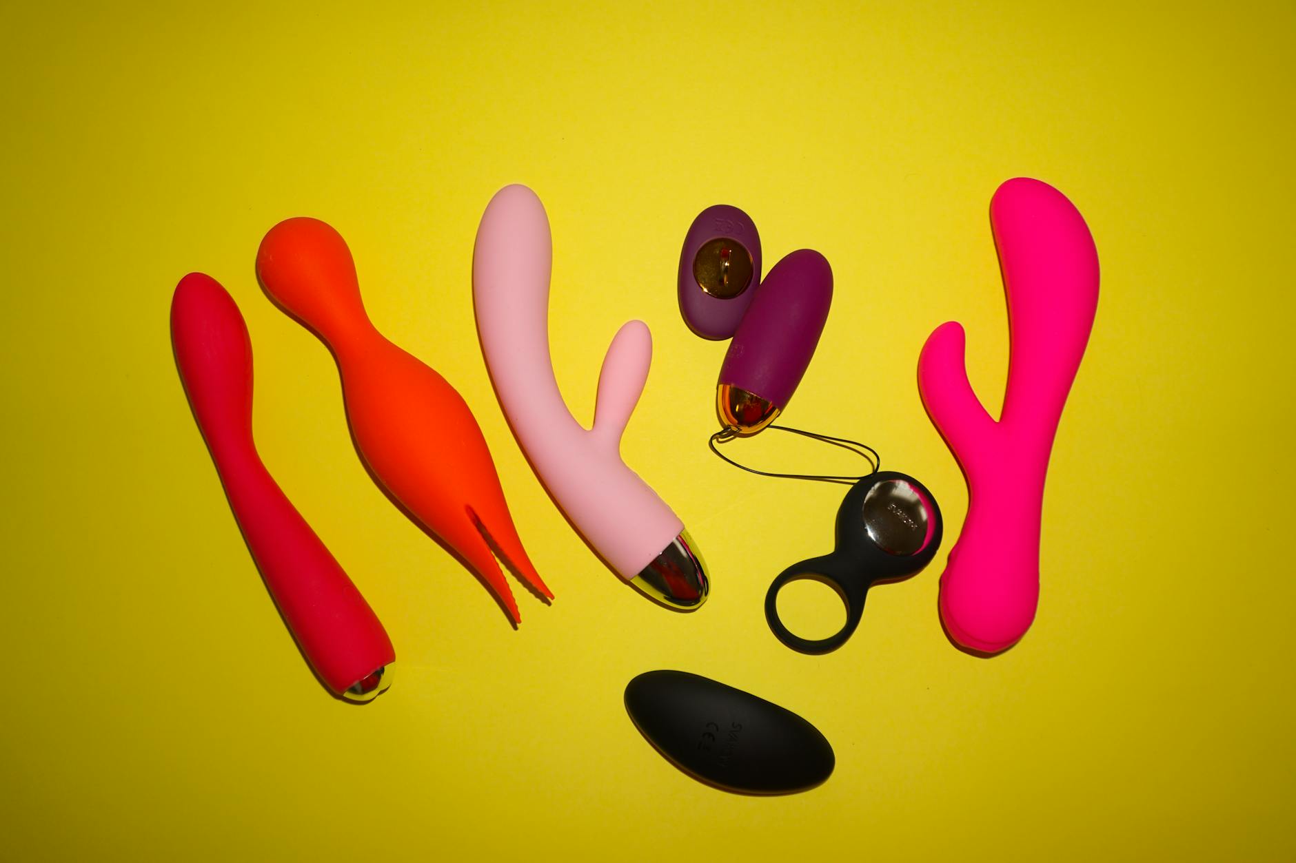 Studio setup showcasing colorful sex toys on a bright yellow background, featuring precision designs for intense pleasure