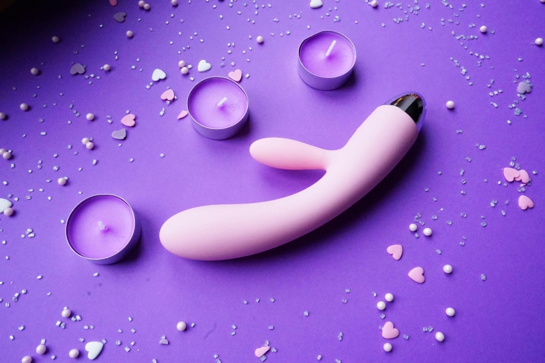 A hand holding a fresh lemon on a soft pink background, symbolizing the bright, concentrated pleasure of lemon vibrators